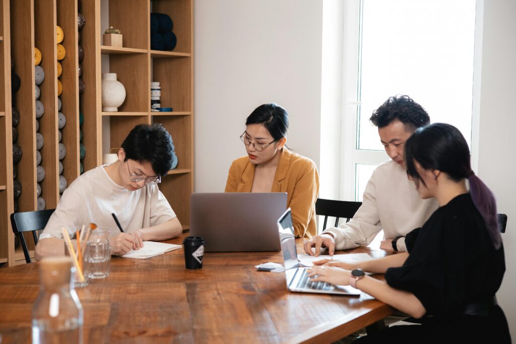 four businessmen sit at a table and work with documents and computers to apply requirements elicitation techniques