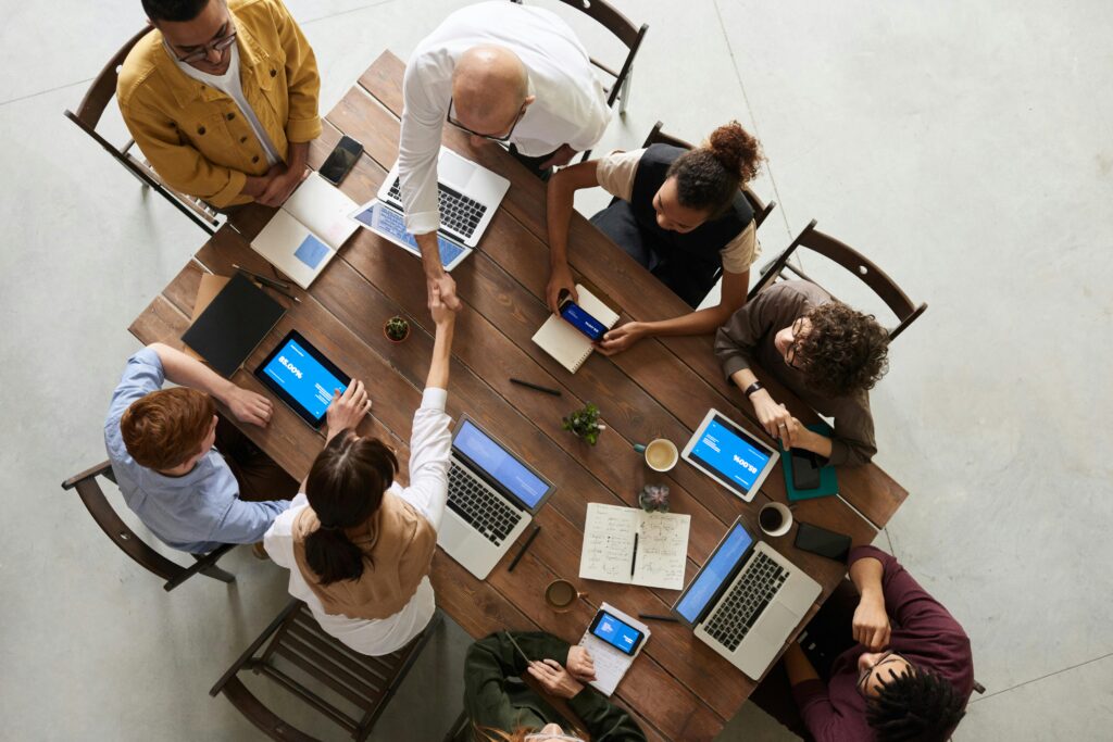 A table with business people from above and two people shaking hands to illustrate understanding and resolving conflicts in requirements elicitation