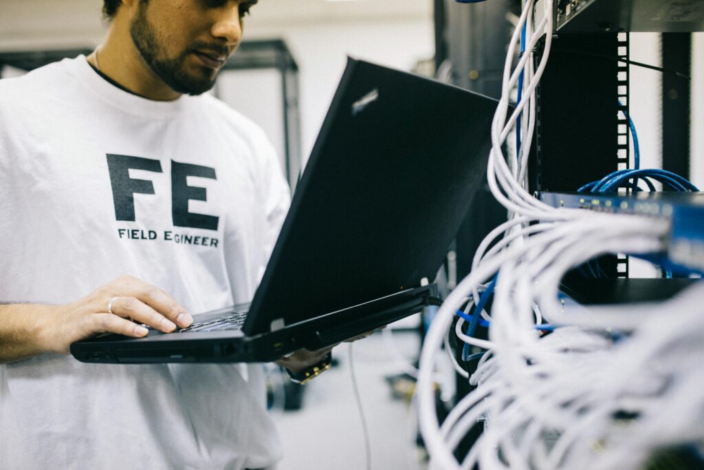 A man stands with an open laptop in his hand in front of a body-high server to illustrate requirements engineering in IT systems