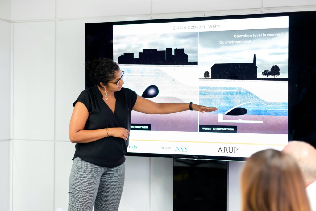 a woman in front of a big screen pointing at graphics illustrating Requirements Engineering Decision Making