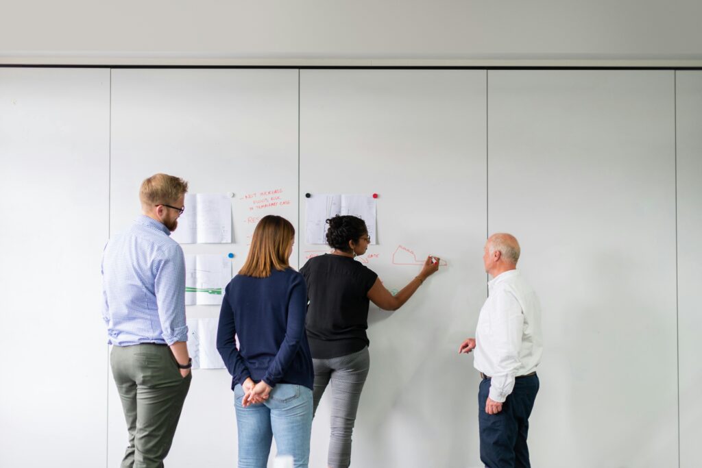 Two women and two men stand in front of a wall on which they write aITIL service strategy as a strategic asset